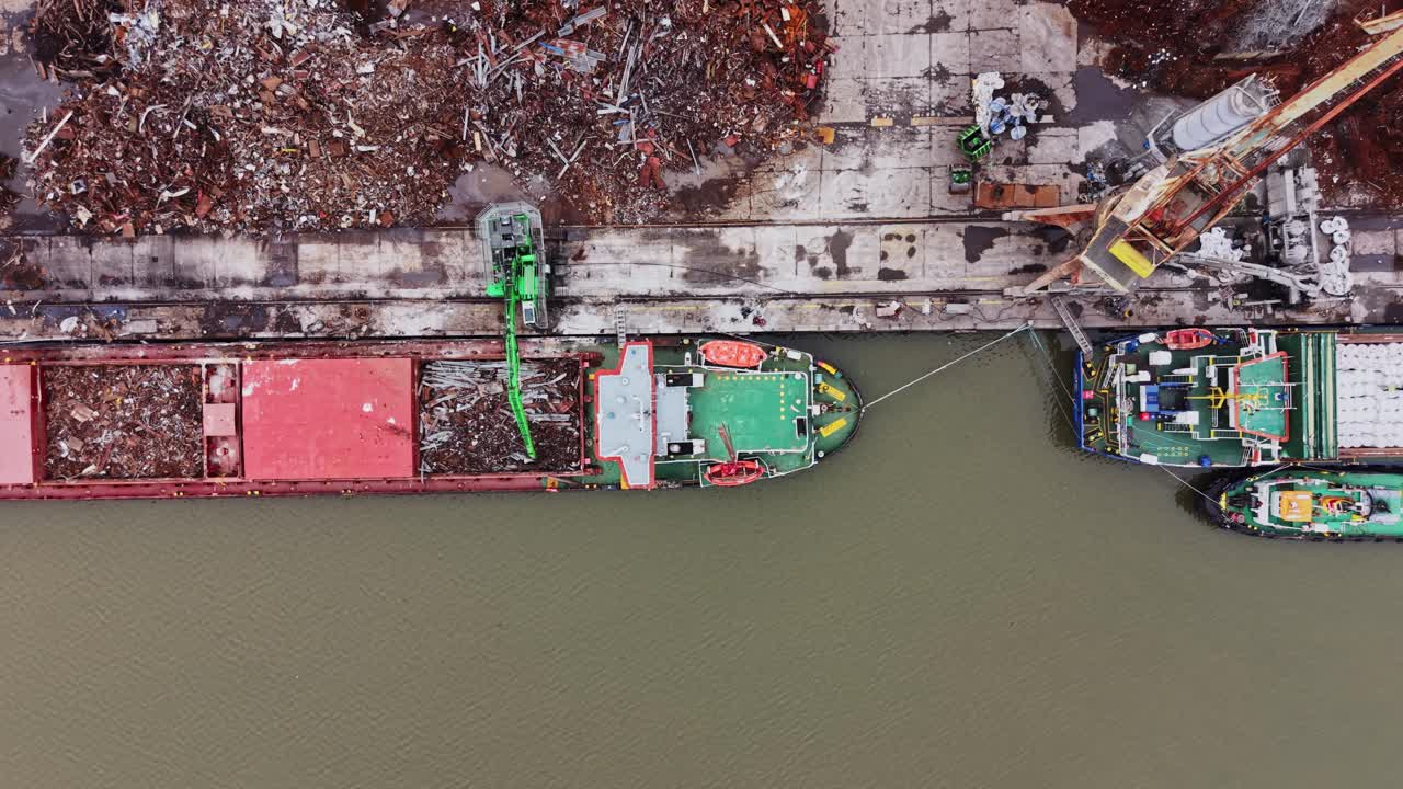 Barco descargando carga en un astillero en una zona industrial concurrida.