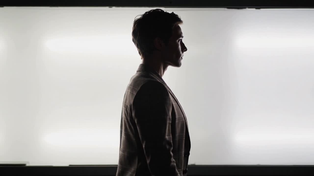 Walking man in profile with camera rolling, crossing studio lightbox, being silhouetted in blazer