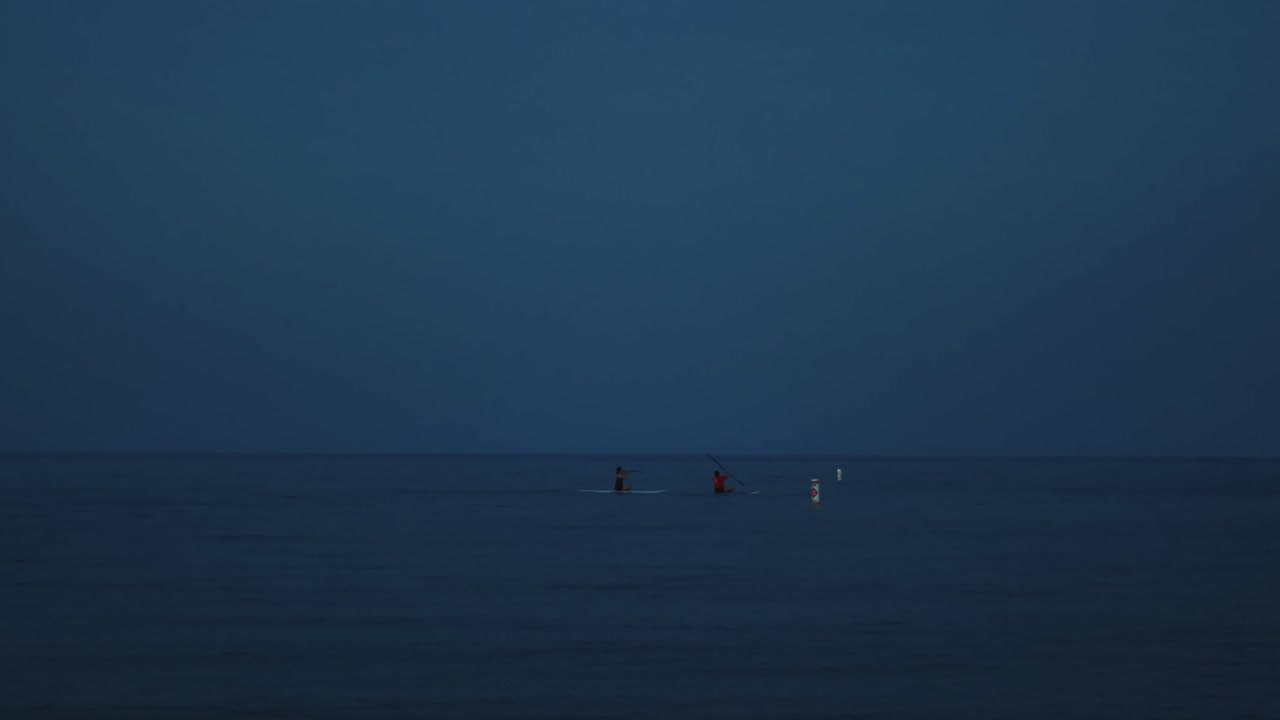 잔잔한 깊고 푸른 바다에서 두 명의 패들 보더가 태양 앞에 있습니다.