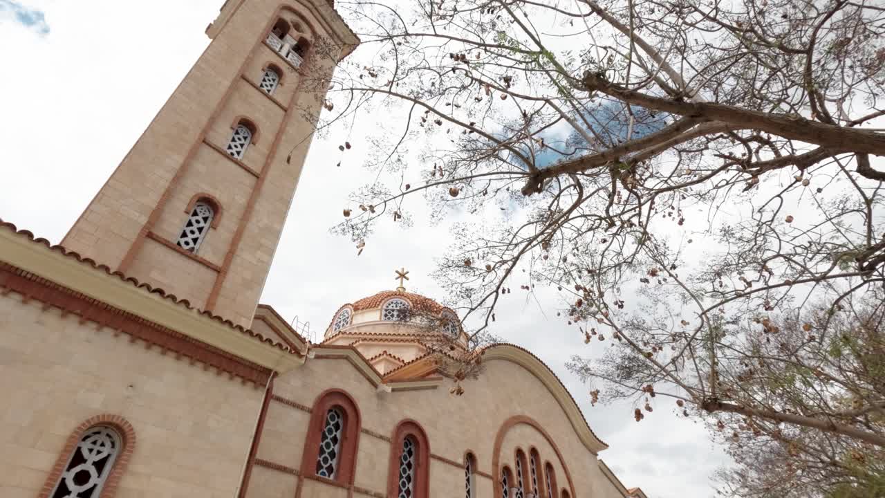 A beautiful church stands tall with its intricate architecture against the backdrop of a cloudy sky. Bare branches frame the scene, creating a serene atmosphere in this peaceful location