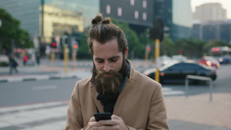 portrait of attractive stylish young bearded hipster man texting browsing using smartphone messaging app in city street