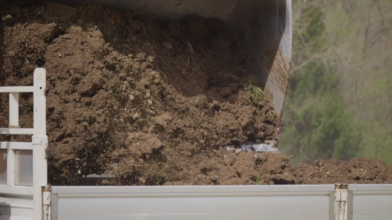 Close-up view when a heavy bulldozer loads earth onto a truck in slow motion.