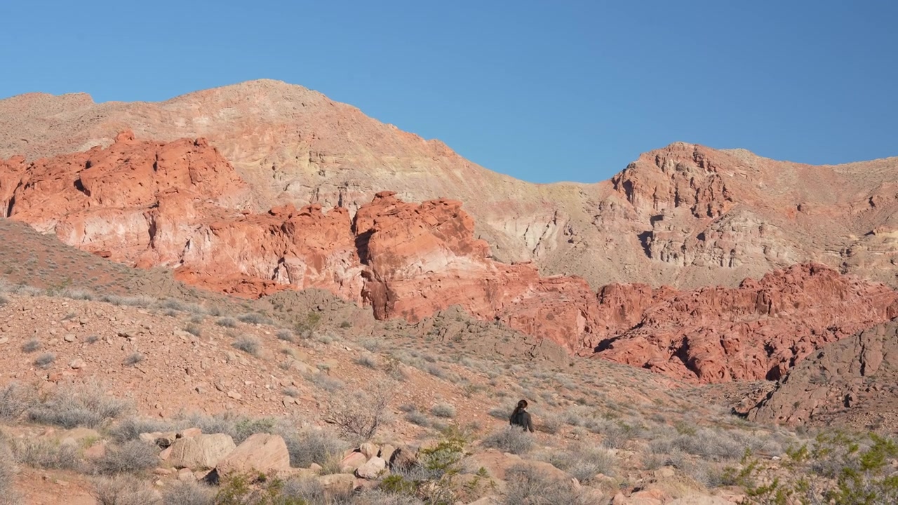 Donna in un paesaggio desertico che cammina su un sentiero davanti a formazioni rocciose di arenaria rossa.