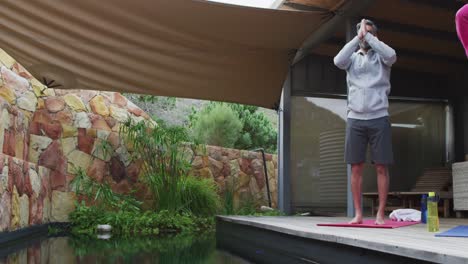 happy diverse couple doing yoga, standing and meditating at terrace