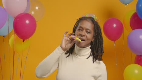 retrato de estudio de una mujer con una cinta para la cabeza de cumpleaños celebrando con globos y soplador de fiesta