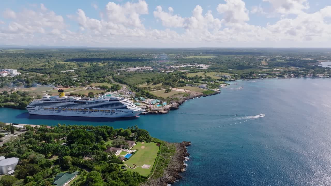 Aerial view of a cruise ship at La Romana Port, Dominican Republic, with coastline and boats. Scenic panoramic aerial, pan left view ship and port.