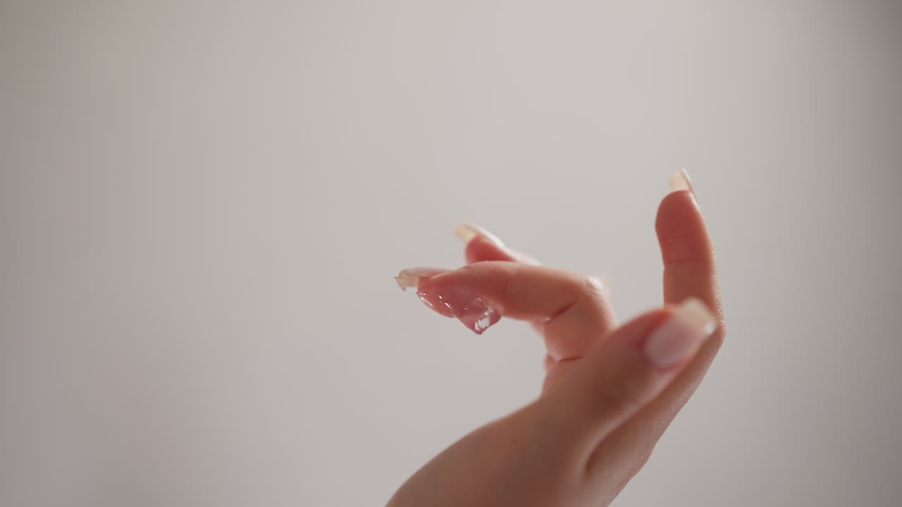 여성은 화장실에서 손가락에 얼굴 크림을 습니다. 누드 매니큐어를 가진 여성은 가운 배경에 손으로 젤리 같은 크림을 부드럽게합니다.