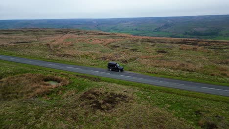 revelación aérea del camión land rover fuera de carretera sentado en la parte superior de los páramos del norte de yorkshire en una larga carretera vacía durante un día nublado con un vasto valle y paisaje en el fondo