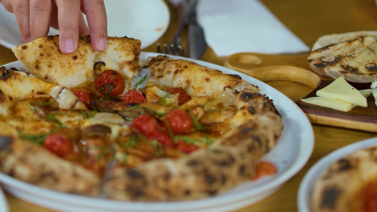 Uma pessoa levanta uma fatia de pizza de forno a lenha de um prato durante um jantar em grupo