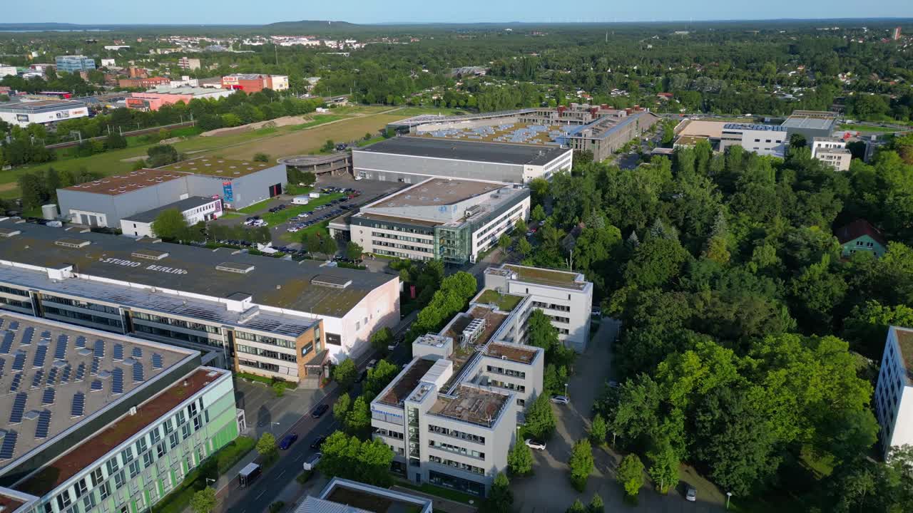 Modern film studios with offices and sound stages surrounded by trees in Berlin Adlershof, Germany. Dramatic aerial view flight overflight flyover drone