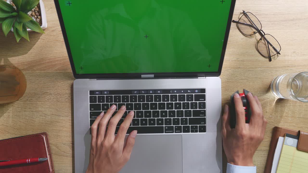 vista de arriba hacia abajo de una computadora portátil con pantalla verde simulada pantalla chromakey en un escritorio de oficina de madera al lado de la libreta con bolígrafos, gafas y un vaso de agua.
