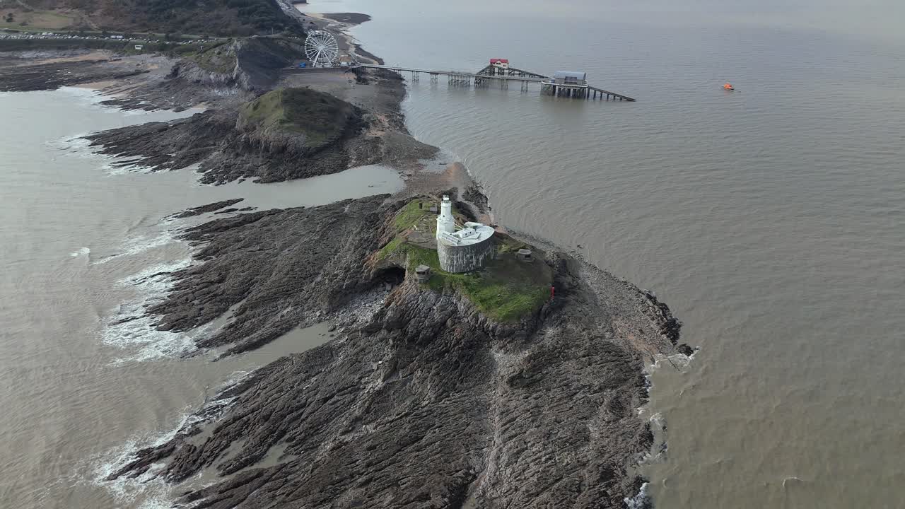 Aerial pan shot of Mumbles Lighthouse in between Swansea on rocky terrain at United Kingdom.
