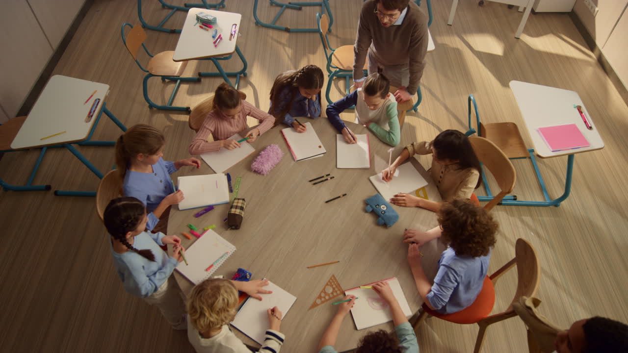 smiling schoolteacher helping students. Scool kids sitting at round desk