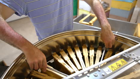 beekeeper rotates the metal bin full of honey frames. man checks-up if all the frames stand right. close up.