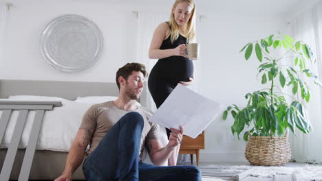 young couple with pregnant woman in bedroom look at instructions for self assembly baby cot