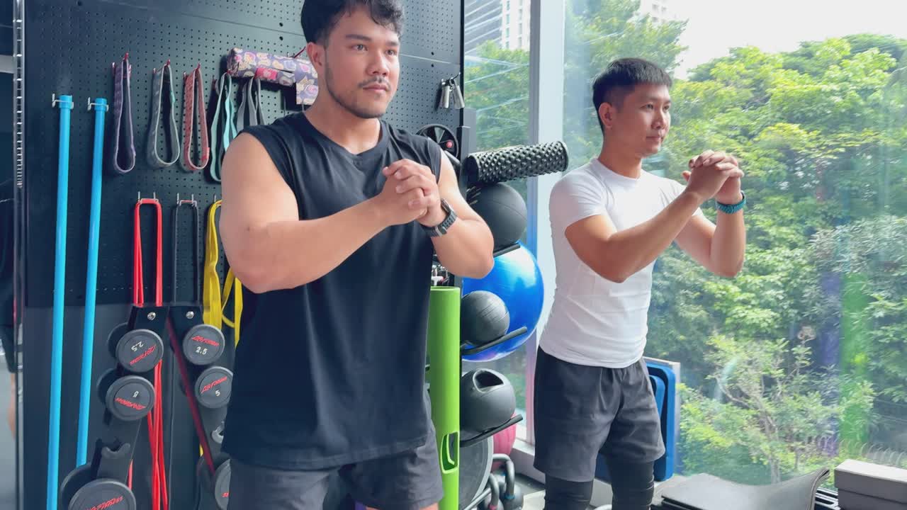 Two people perform squats in a modern gym, focusing on strength, technique, and natural lighting