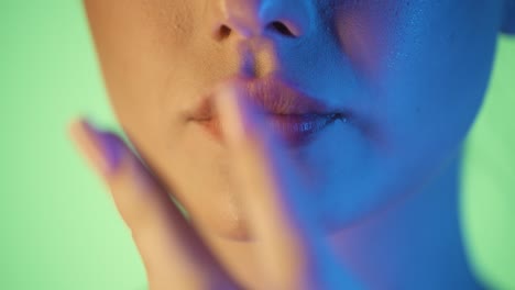 extreme close up shot of beautiful woman lips of a young woman who has eaten delicious food and strokes her lips with her finger in front of green background with blue contrast in her face