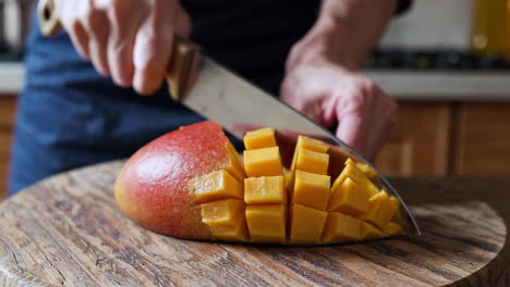 person cutting a mango into cubes on a wooden board