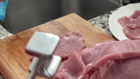 tenderizing pork with meat mallet tool - using meat tenderizer meat pounder to prepare slabs of pork and seasoning with salt for por schnitzels recipe at home in kitchen slow motion slo-mo