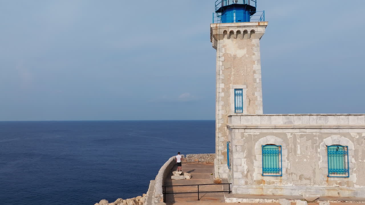 Side angle of Tainaron Lighthouse beside cliffs, dramatic seascape in soft late light, aerial