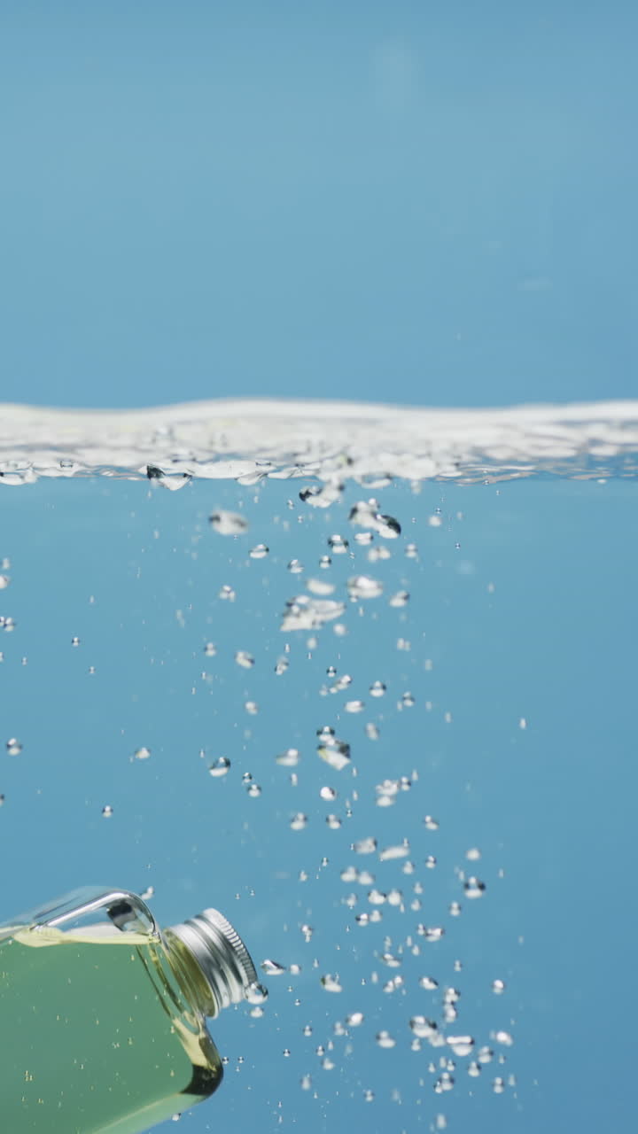 Vertical video of beauty product bottle falling in water with copy space on blue background