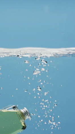 vertical video of beauty product bottle falling in water with copy space on blue background