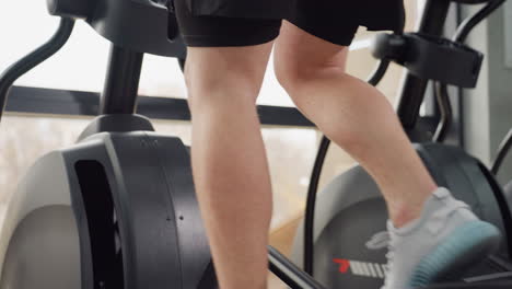 back view of sporty man powering treadmill with swift leg motion showcasing muscular calves dynamic energy during indoor cardio workout in modern gym environment by large bright windows