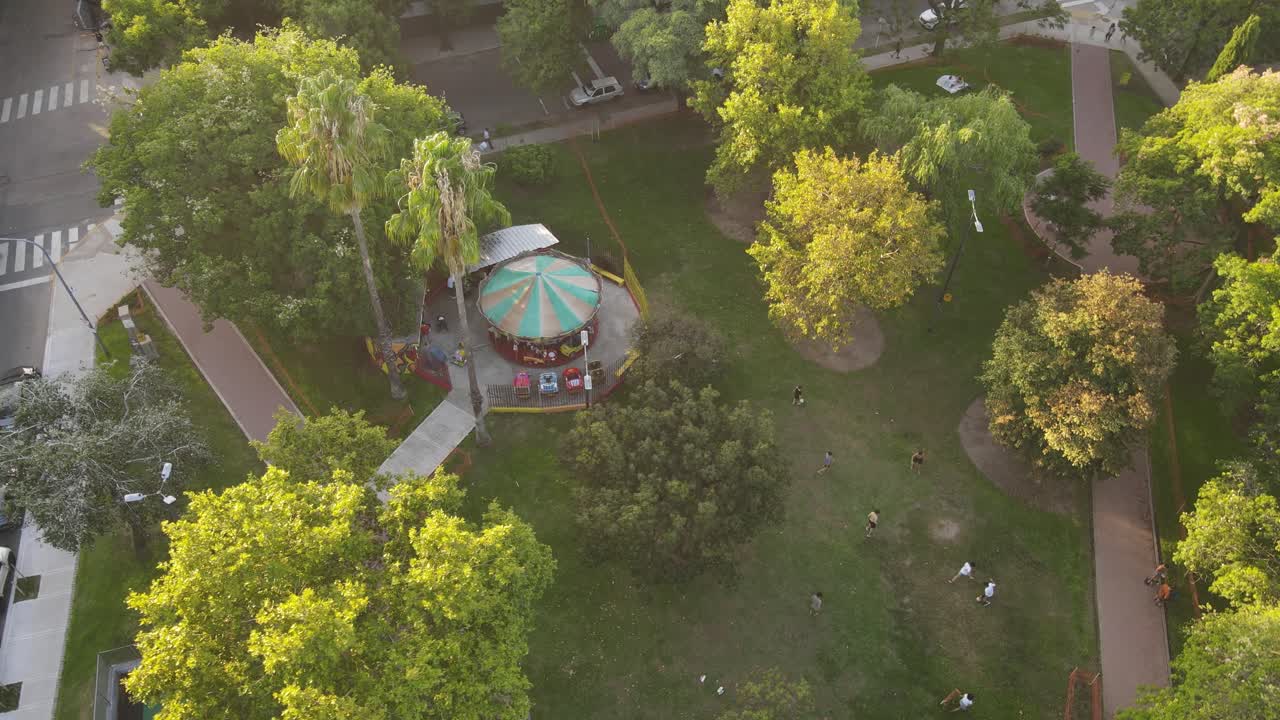 parte superior aérea hacia abajo del carrusel giratorio en el parque tropical a la hora de la puesta del sol - la gente caminando por el camino en la ciudad de buenos aires