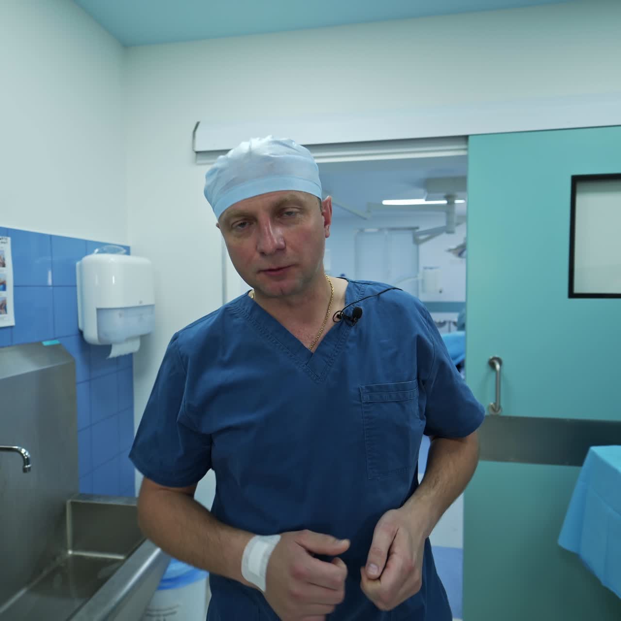 Middle-aged surgeon leaving the operational theatre. Doctor takes off the mask and coat and speaks to the camera
