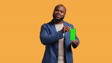 Cheerful-man-recommending-green-screen-smartphone,-studio-background