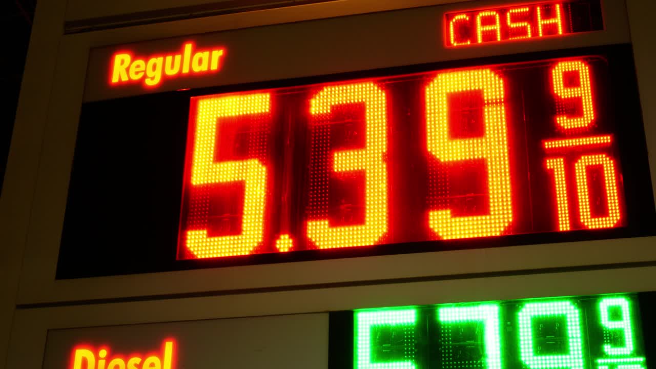 Gas station prices LED light up sign for regular and diesel fuel at night over 5 dollars per gallon credit and cash price, during 2021 2022 war time recession, ground up shot panning left to right