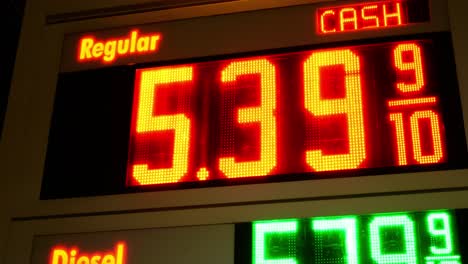 gas station prices led light up sign for regular and diesel fuel at night over 5 dollars per gallon credit and cash price, during 2021 2022 war time recession, ground up shot panning left to right