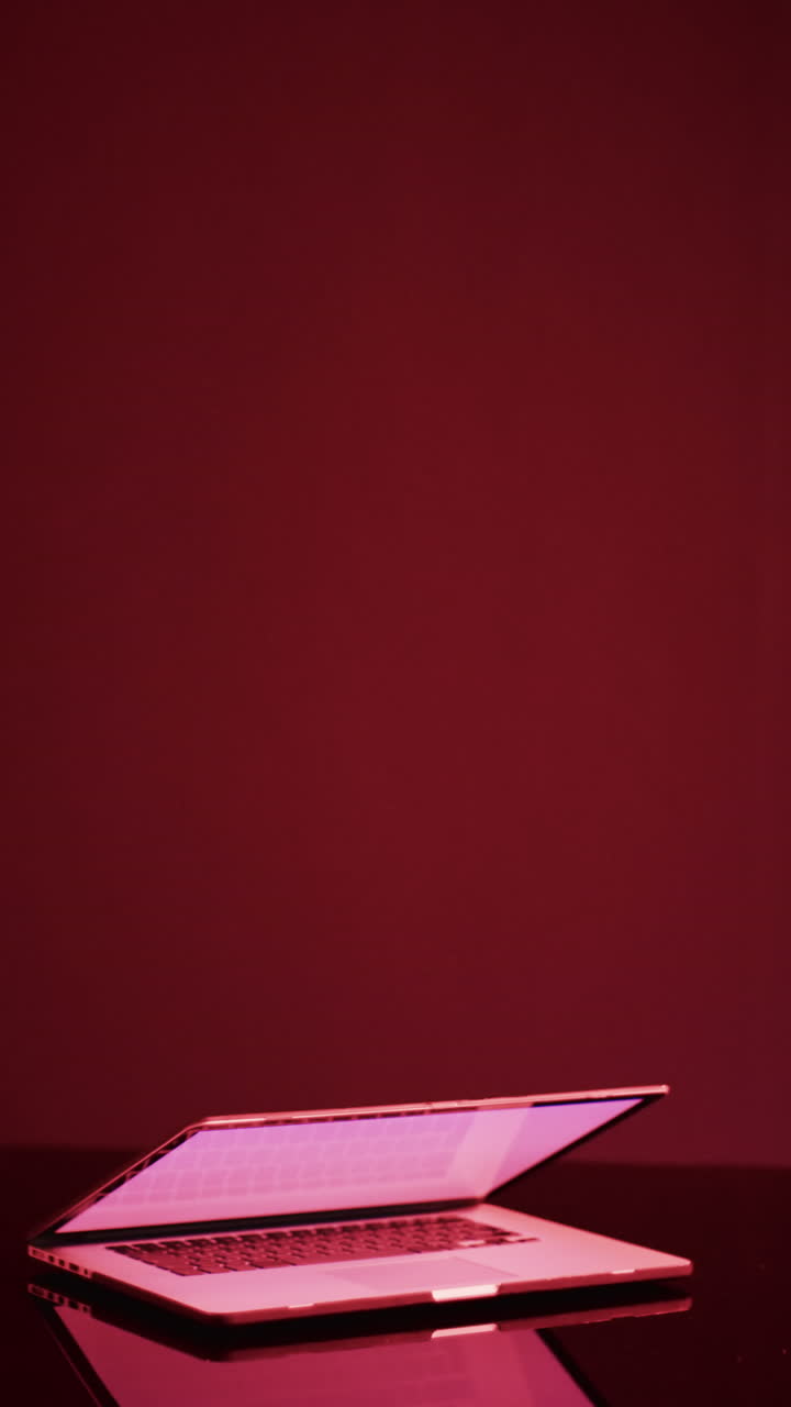 Vertical video of laptop with blank screen on red neon background