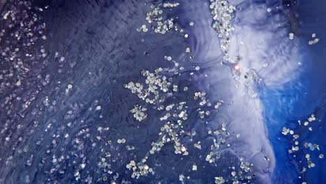 macro shot of blue ink dispersing in water with white particles, resembling a cosmic galaxy