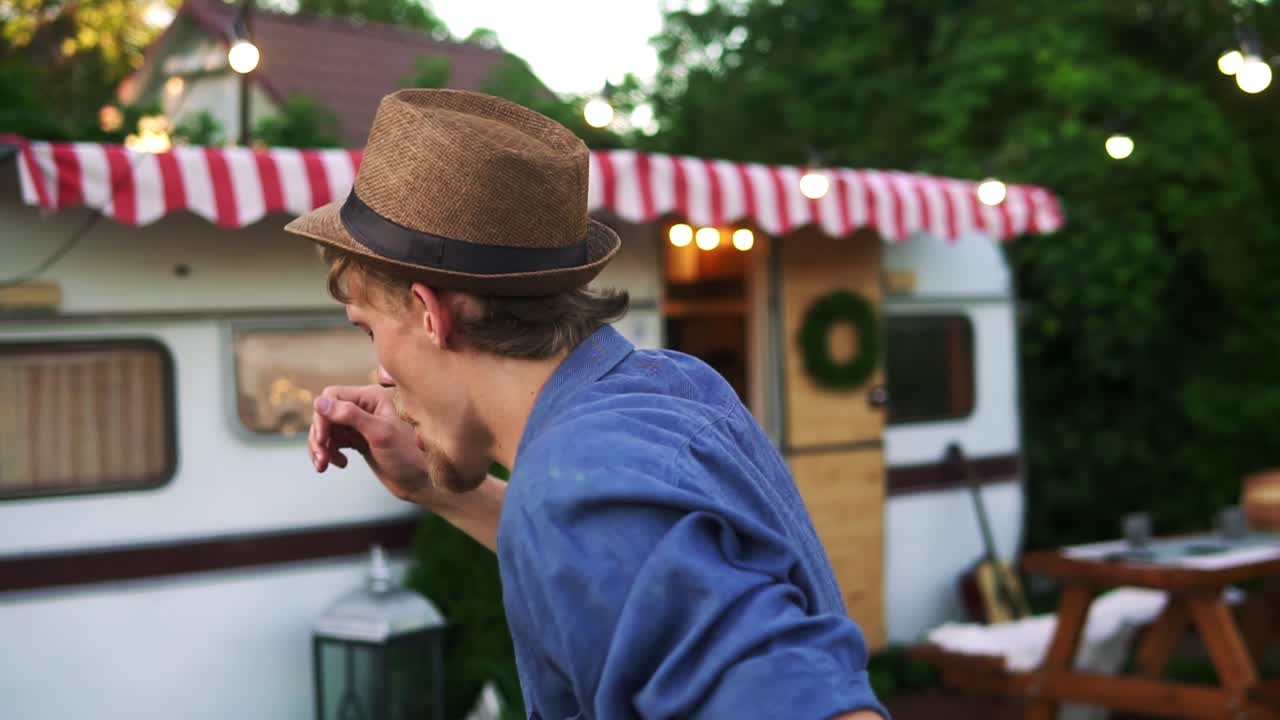 Happy cheerful man in casual clothes and summer hat is dancing outdoors in front the trailer truck. Bearded joyful man in his best mood, dancing happily. Slow motion