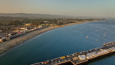 santa cruz california aerial v11 cinematic flyover wharf pier panning towards popular beach boardwalk entertainment complex and outdoor amusement park at sunset - shot with mavic 3 cine - may 2022