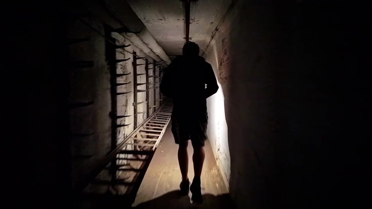 Un uomo cammina nell'oscurità di un misterioso tunnel nel seminterrato di una fabbrica senza luce, illuminandosi con una lampada