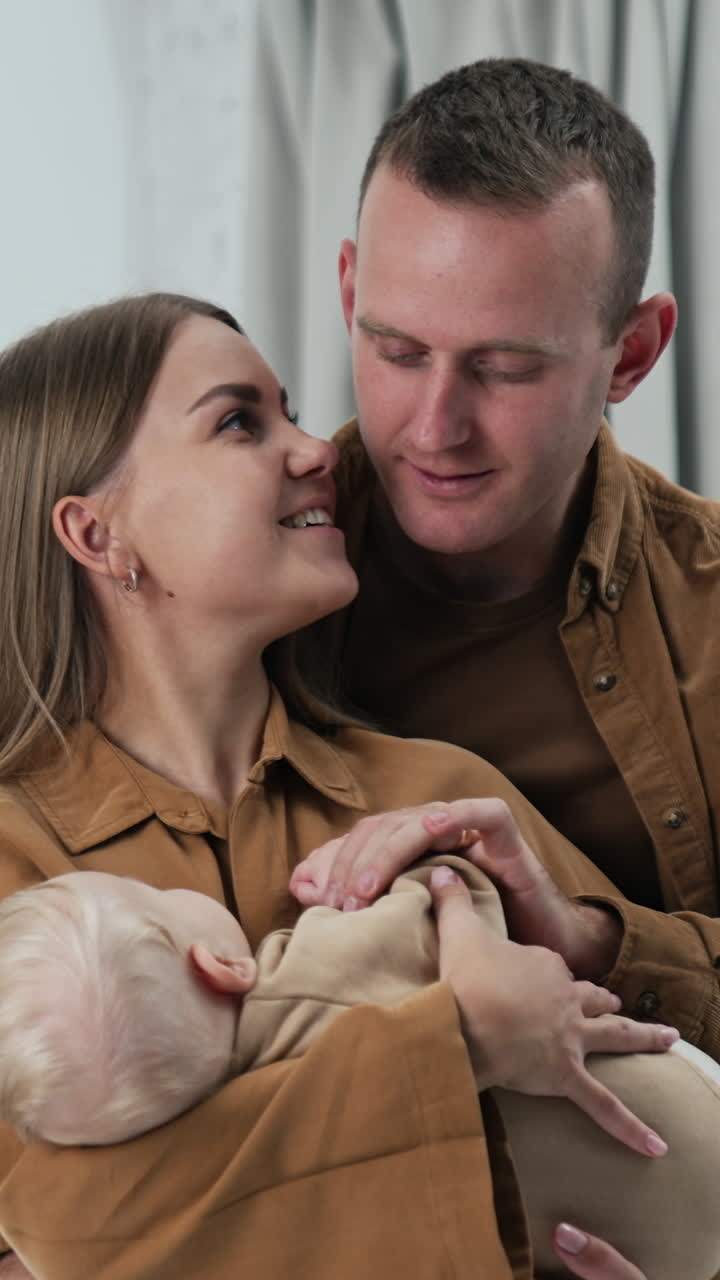 Mother swaying her little infant child. Loving husband stand behind stoking his wife and takes baby hand to kiss. Vertical video