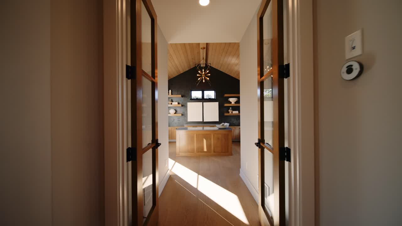A minimalist modern office with large windows, wooden ceiling, and built-in shelving, featuring a central island and natural light streaming through the windows
