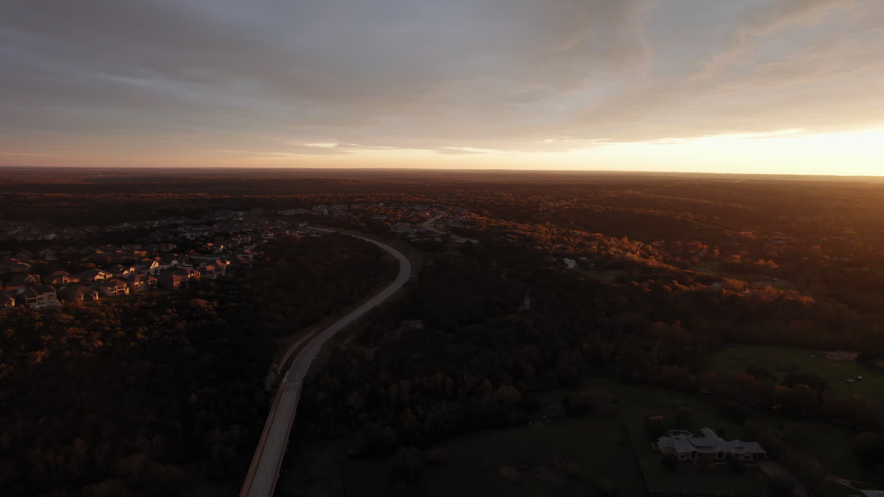 fotografía aérea sobre un suburbio estadounidense al atardecer, dolly lateralmente sobre una carretera ancha