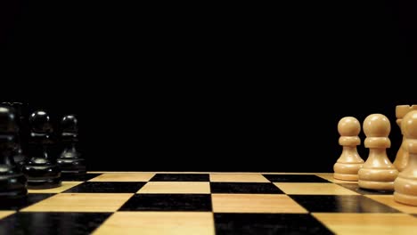 dolly shot backwards along the chess pieces standing on either side of the chessboard against a black background