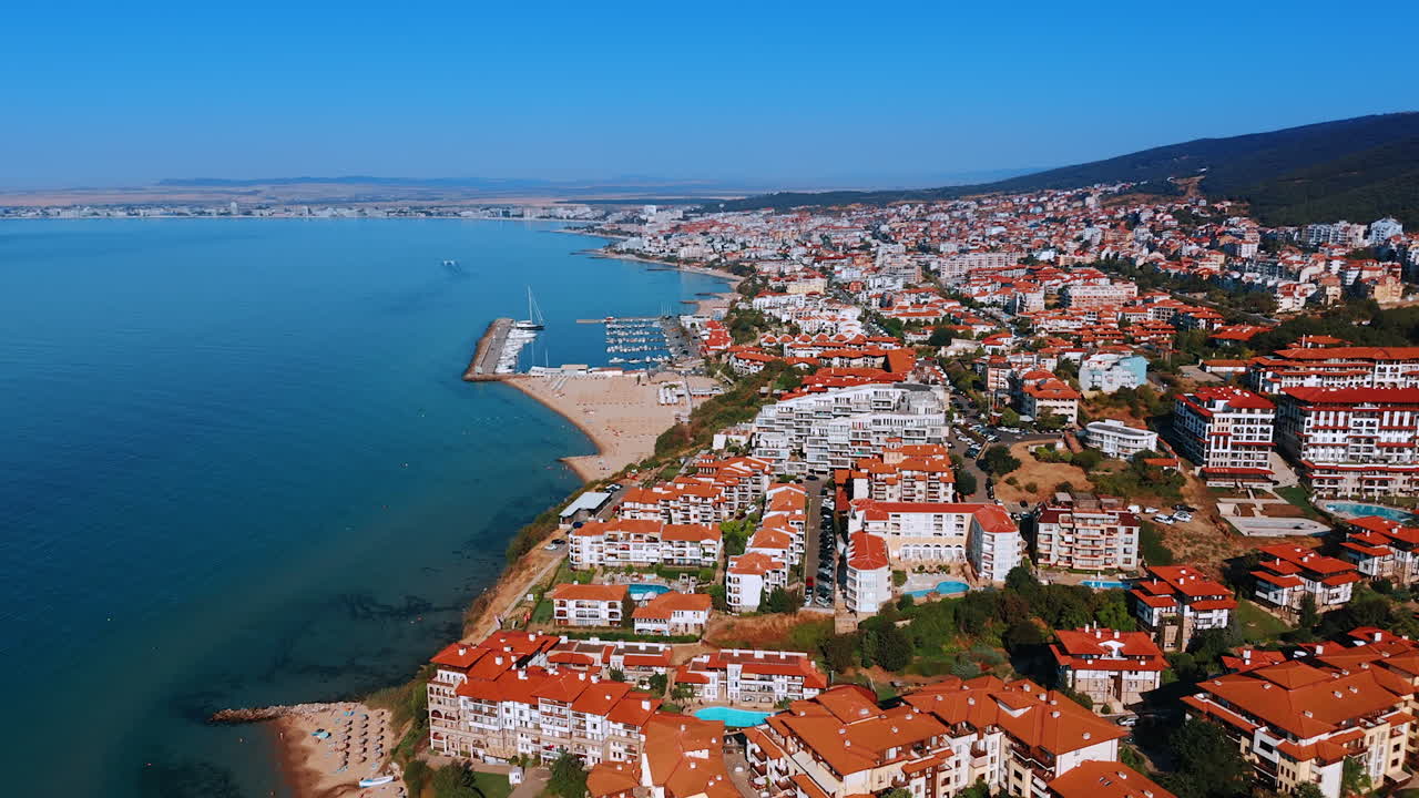 Coastal view of a vibrant seaside town. A scenic coastal view featuring a busy marina, sandy beach, and colorful buildings under a clear blue sky