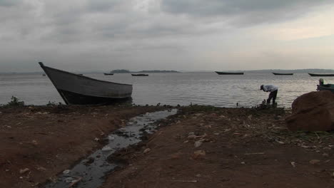 medium shot of a fisherman working on the shores of lake victoria uganda near boats