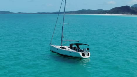 Dando-Vueltas-A-Un-Yate-De-Vela-Blanco-En-Las-Increíbles-Aguas-Tropicales-Del-Océano-Azul-Frente-A-La-Costa-De-La-Playa-De-Whitehaven-En-Queensland,-Australia