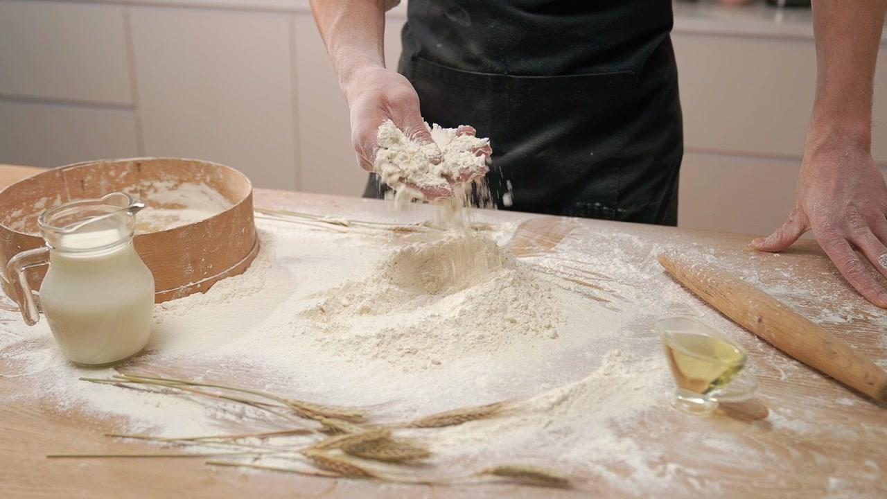 Mani dello chef che versano farina su un tavolo di legno per infornare