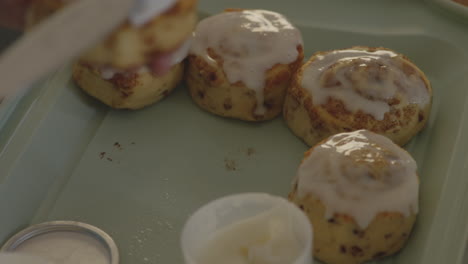 close up slow motion shot of a person frosting fresh, homemade cinnamon rolls