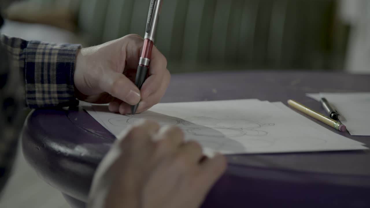 Sketch artist drawing shapes on purple table with sketch pencil.