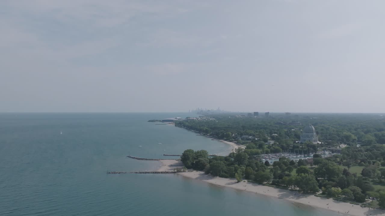 Wide aerial footage moving forward of the coast of Lake Michigan with the Baháʼí House of Worship in the foreground and Chicago in the hazy background