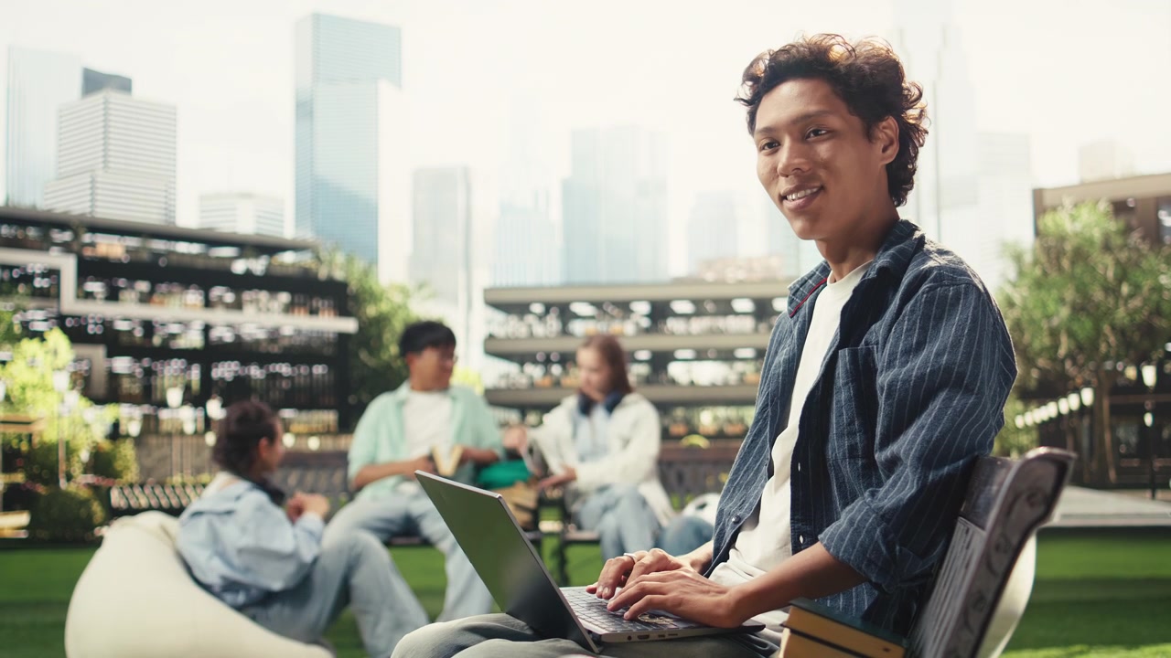 微笑的學生在木製長椅上輕鬆地使用手提電腦工作
