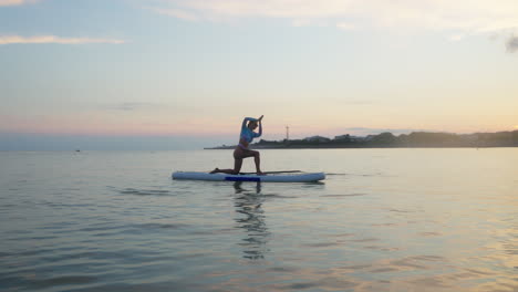 mujer practicando yoga en un paddleboard de pie al atardecer